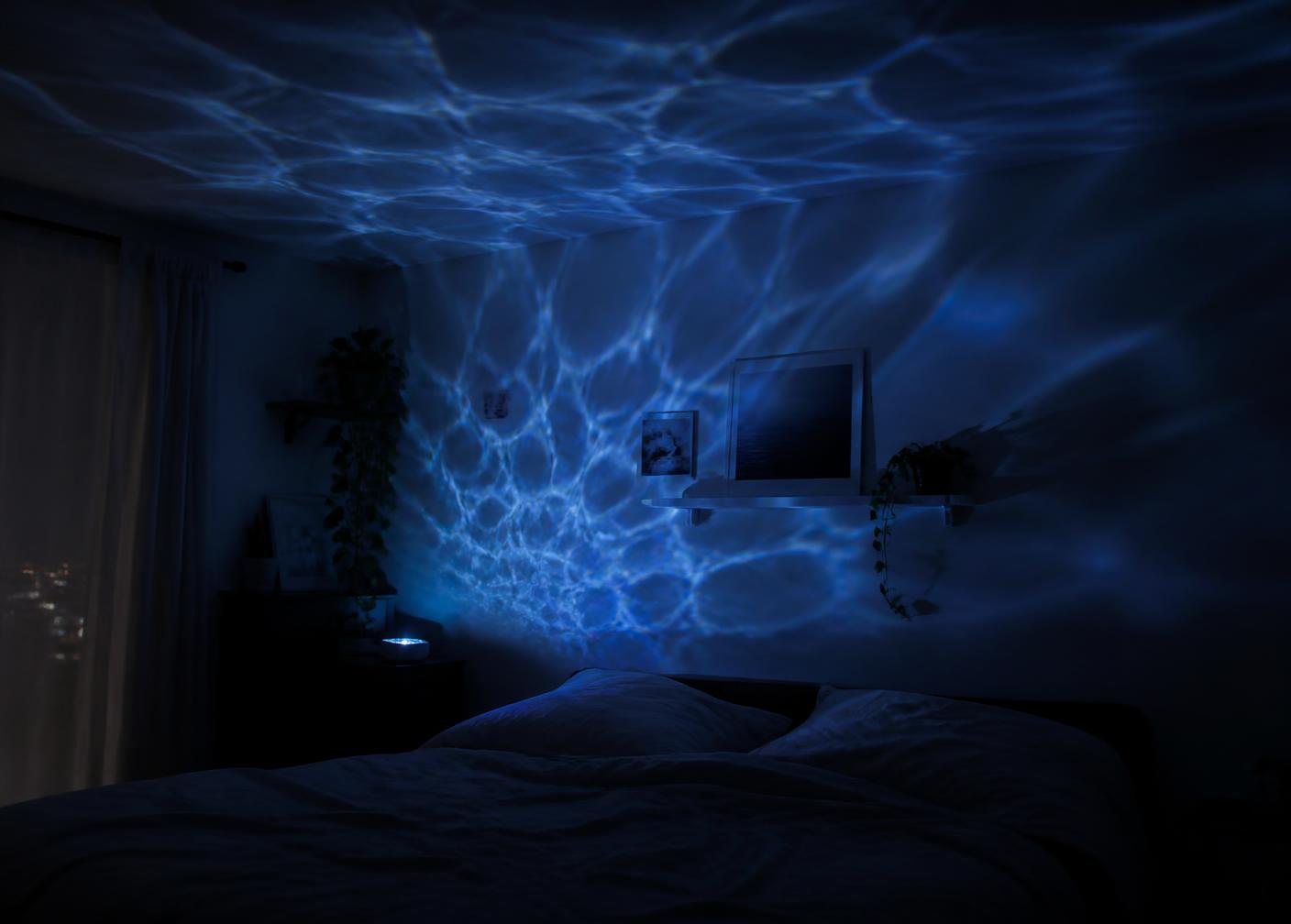 Blue ocean wave light ripples projected across a dark bedroom wall and ceiling